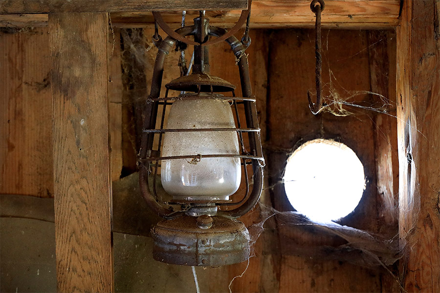 The corner of an old wooden shed with a hanging lamp and cobwebs.