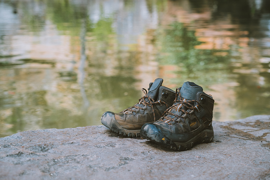 A pair of hiking boots sitting on a rock by a body of water.