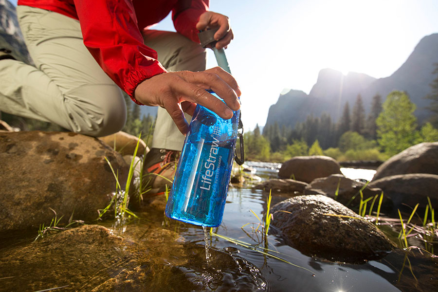 A hand filling up a blue bottle from a stream.