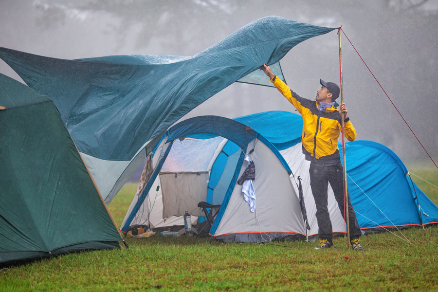 A man attempts to steady his tent's shelter in heavy wind and rain. 
