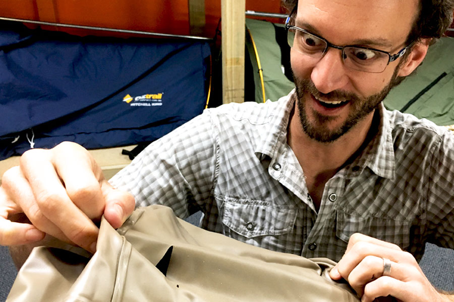 A man is gaping at a tear in the material of his tent. 