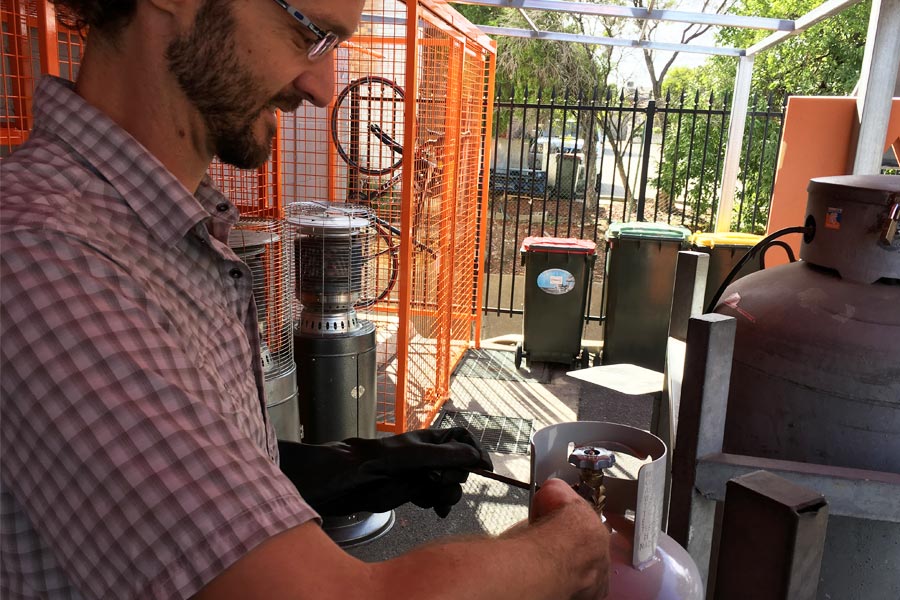 A man fills a gas bottle, with an orange fence in the background.