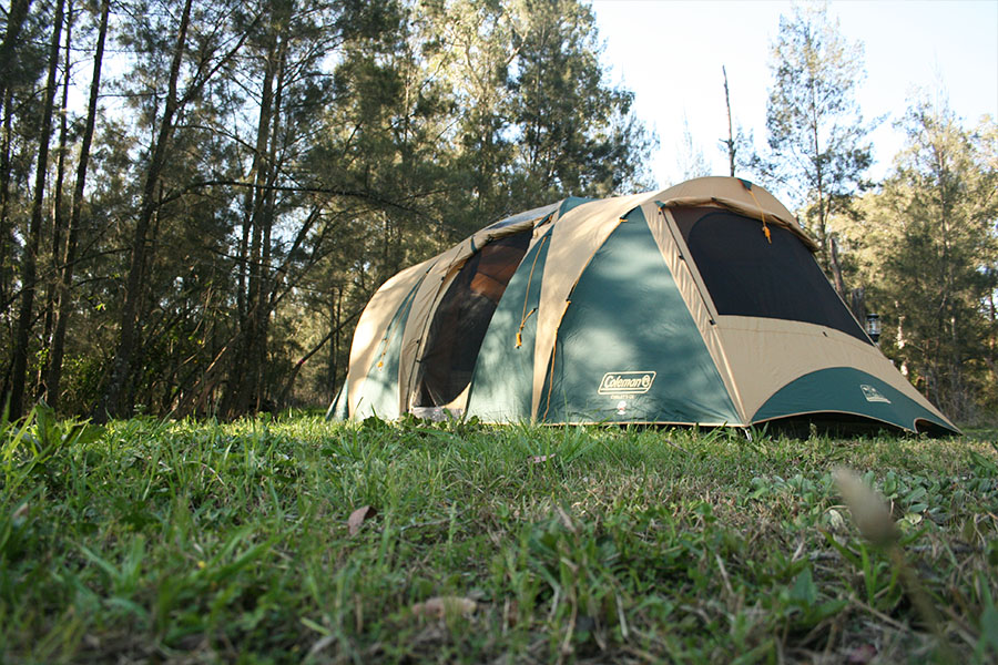 A family tent set up on green grass, with trees in the background.