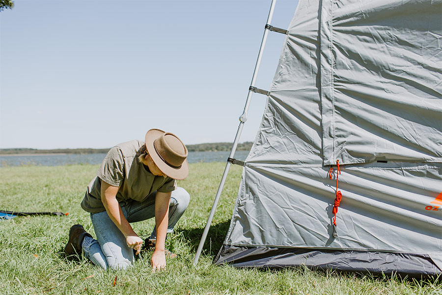 A camper hammering in a peg to pitch a tent.