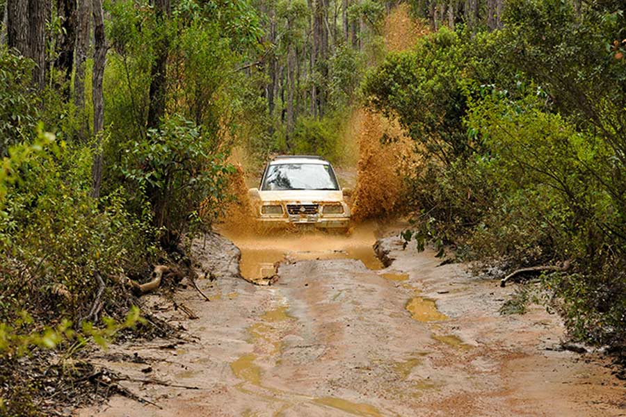 An old Suzuki Vitara driving through a muddy puddle