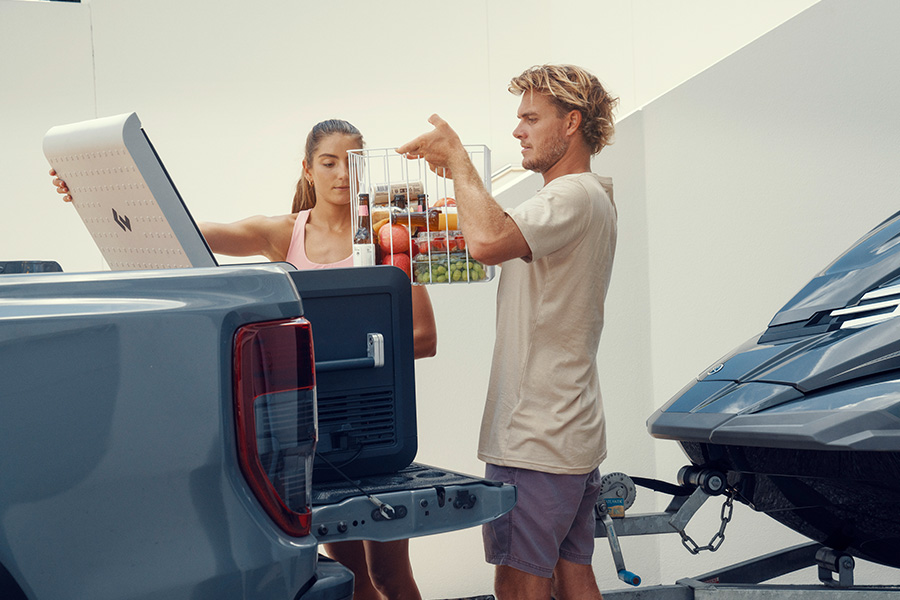 A couple are loading a crate of food into a portable fridge.
