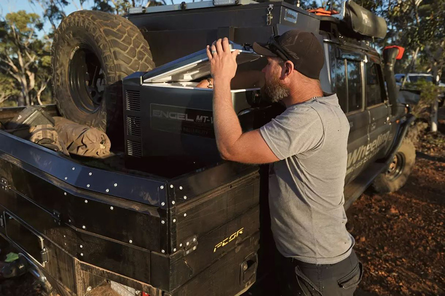 A man peeking into his fridge in the back of his vehicle. 
