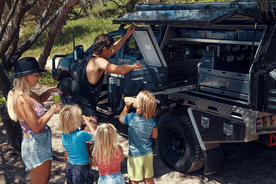 A man fetching drinks and iceblocks from an icebox for three children.