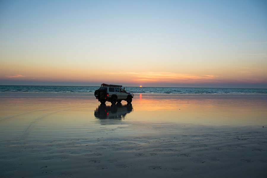 A 4WD on a beach at sunset.