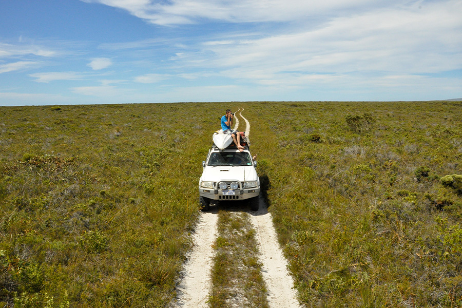 A man sitting on top of his 4WD with a camera, in the middle of a grassy field. 