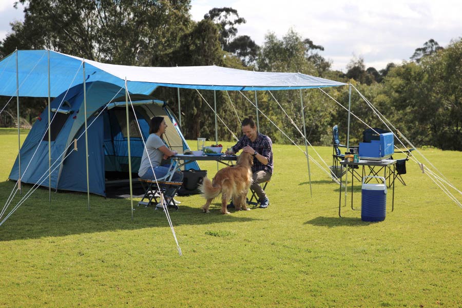 A couple and their dog enjoying the shade of a tarp set up over their campsite