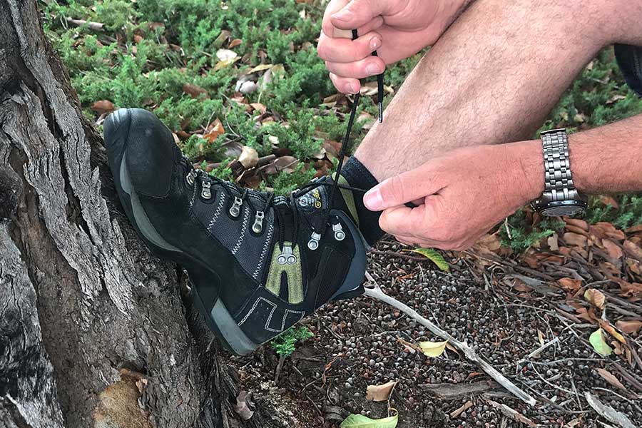 Man lacing up boots on a tree outdoors