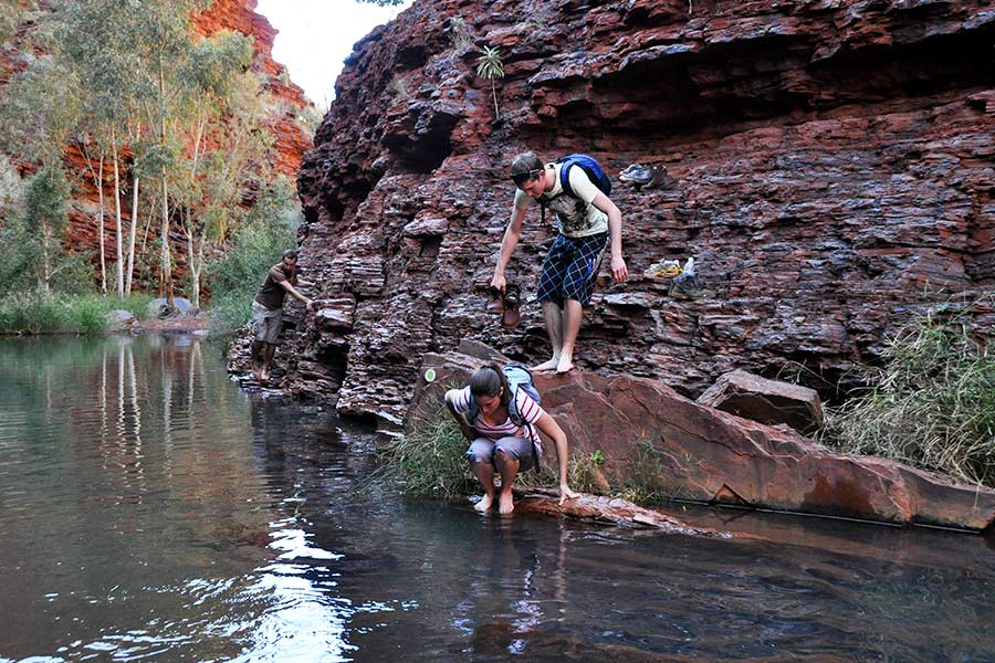 Two young people climbing down some rocks into a creek.