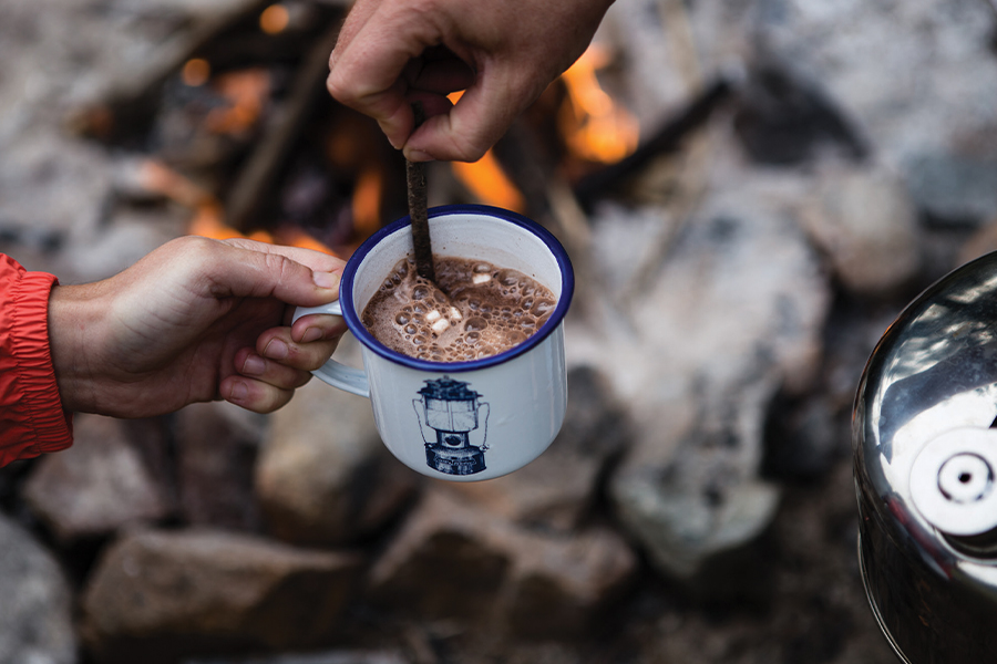 Stirring a mug of hot chocolate over a campfire. 