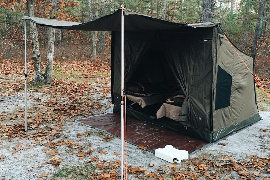 A tent set up on solid ground, surrounded by fallen leaves. 