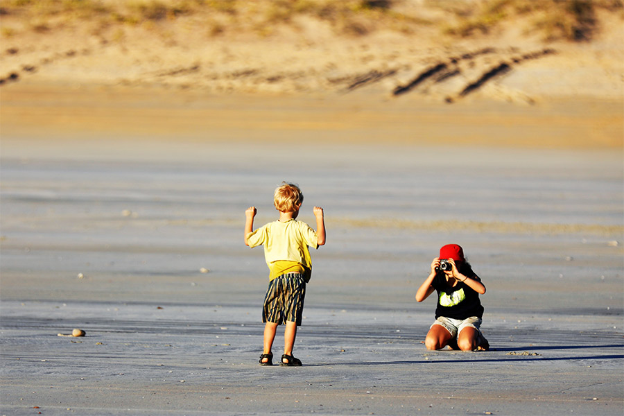 A kid taking a photo of another kid posing at the beach