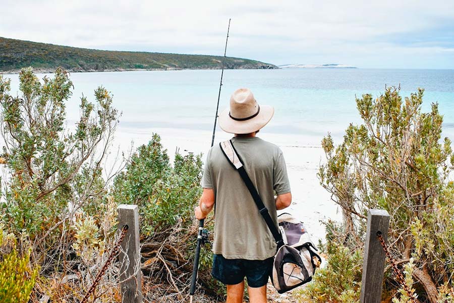 Man walking towards beach with fishing gear