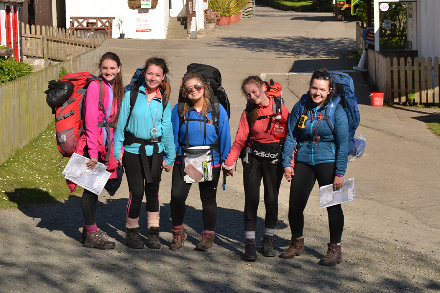 A group of teenage girls wearing packs and hiking boots. 