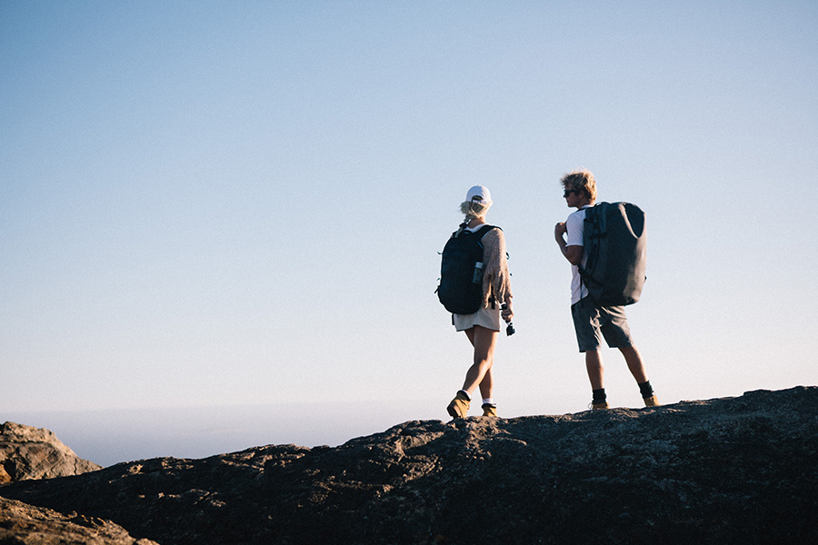 Two teenagers standing on the top of a rock wearing packs. The sky is clear blue. 