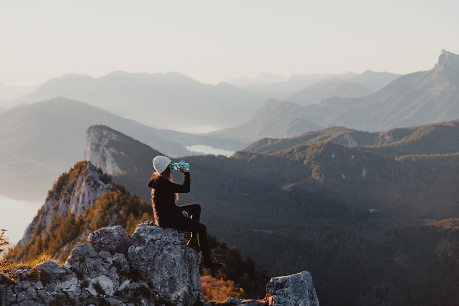 A girl sitting on a rock drinking from a water bottle.