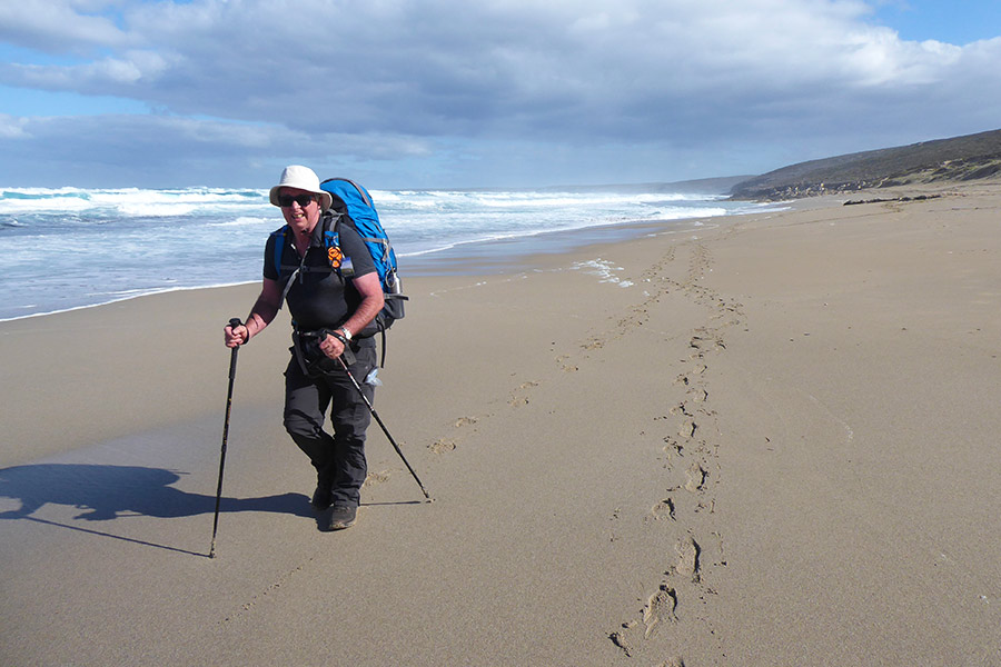 Hiker walking with pack & hiking poles on the beach in KI, South Australia