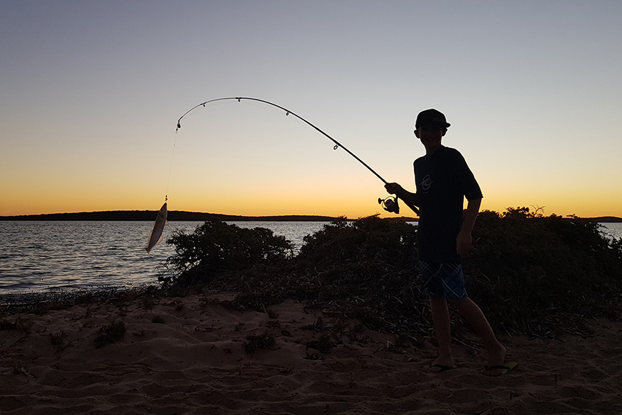 Boy holding fishing rod at night with fish on the end of the line