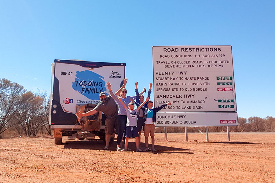 Family posing for photo with caravan next to a road restrictions sign in the outback