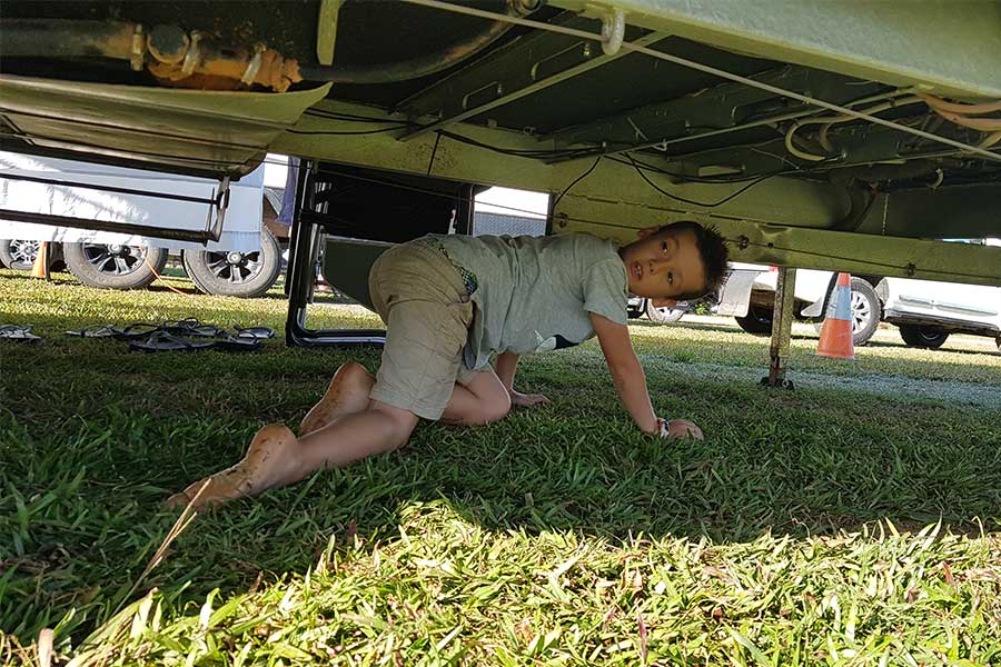 Boy crawling under caravan looking for leaks