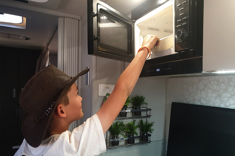 Boy putting food into caravan microwave