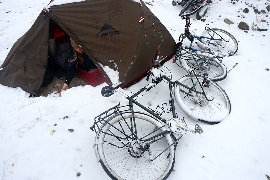 Woman pushing snow out of her hiking tent near her two bikes