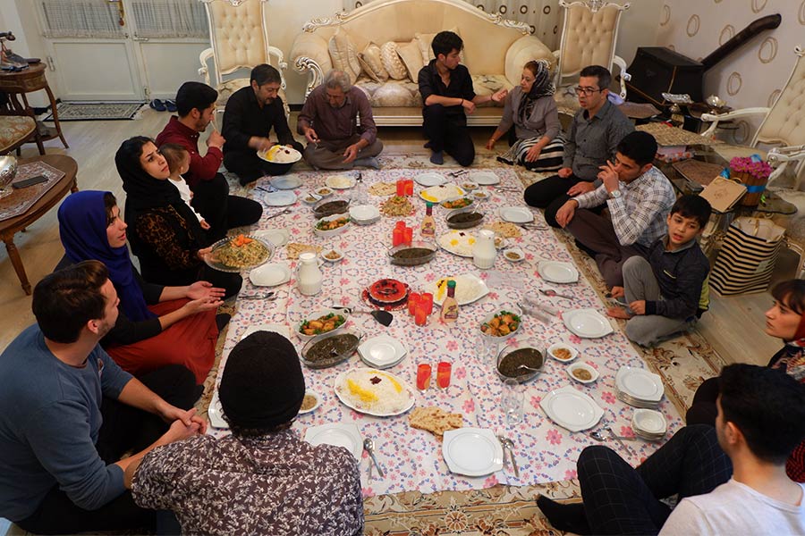 People kneeling around a long sheet in the shape of a dinner table whilst eating