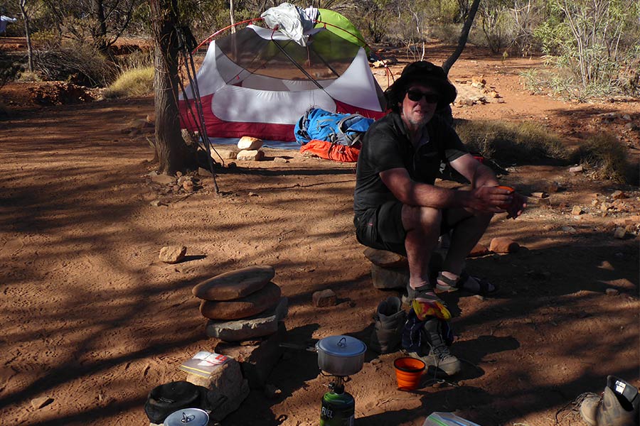 Man sitting on stone stool at his campsite along the Larapinta Trail