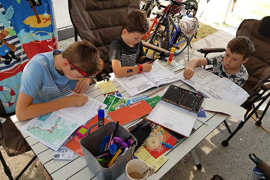 Three young boys studying at a camp table