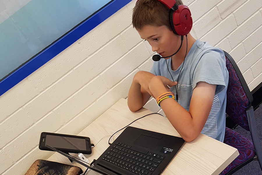 Boy wearing headphones and watching his computer, participating in online school lessons.