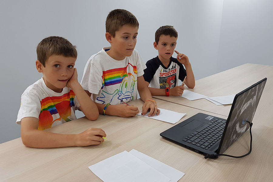 Three boys watching and listening to laptop, participating in distance education