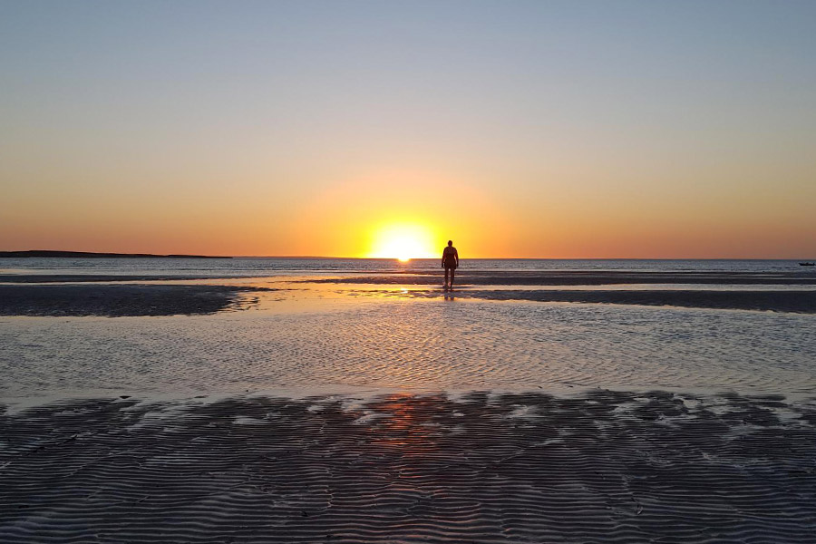 Person walking out during low tide to the ocean with the sun setting in the background at Perlubie Beach in South Australia