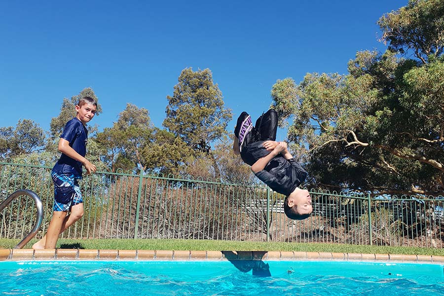Boys jumping into an outdoor swimming pool