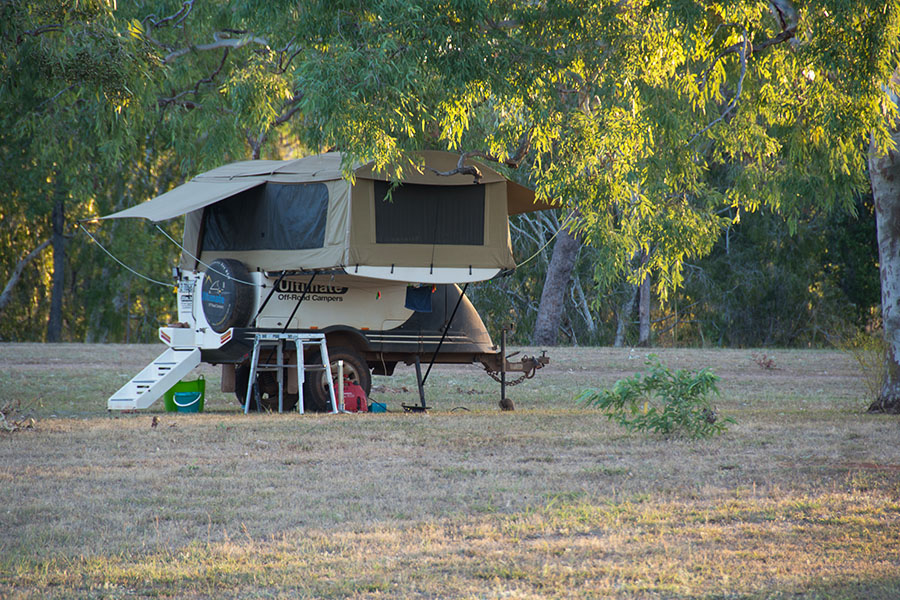 A camper trailer set up on a grassy area beneath some trees.