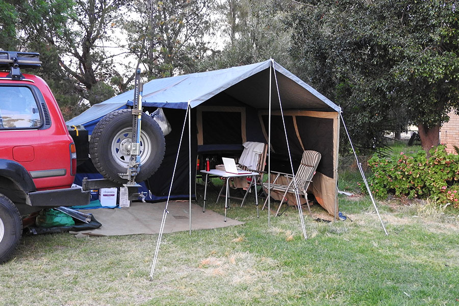 A red 4WD with a camper trailer, table, and chairs set up.