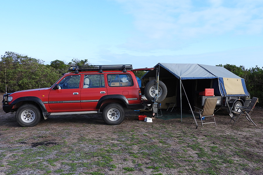 A red 4WD with a camper trailer and chairs set up.