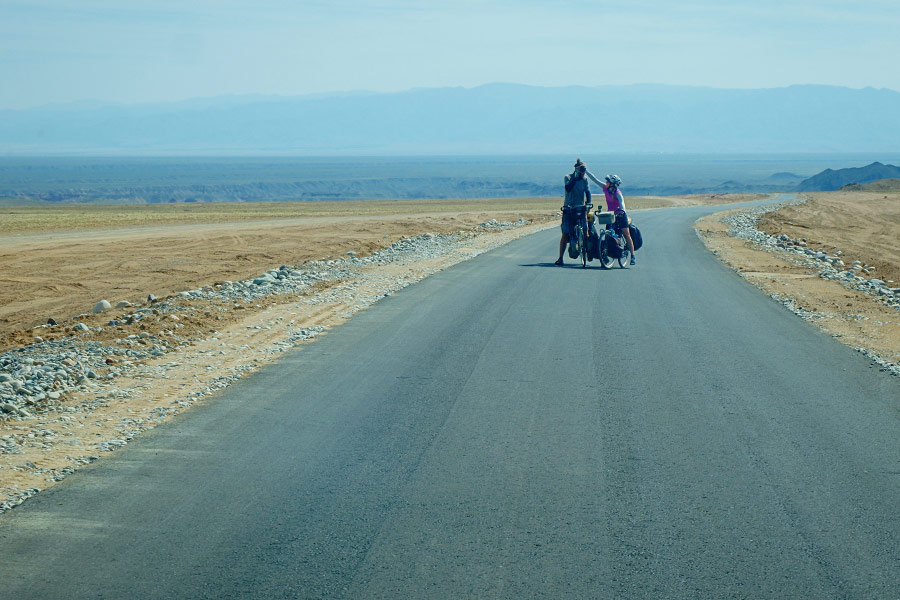 Couple riding their bikes on a rural road in the Desert of Kazakhstan