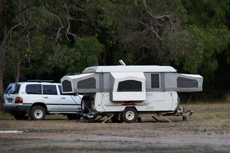 A pop-top camper trailer setup next to vehicle outdoors