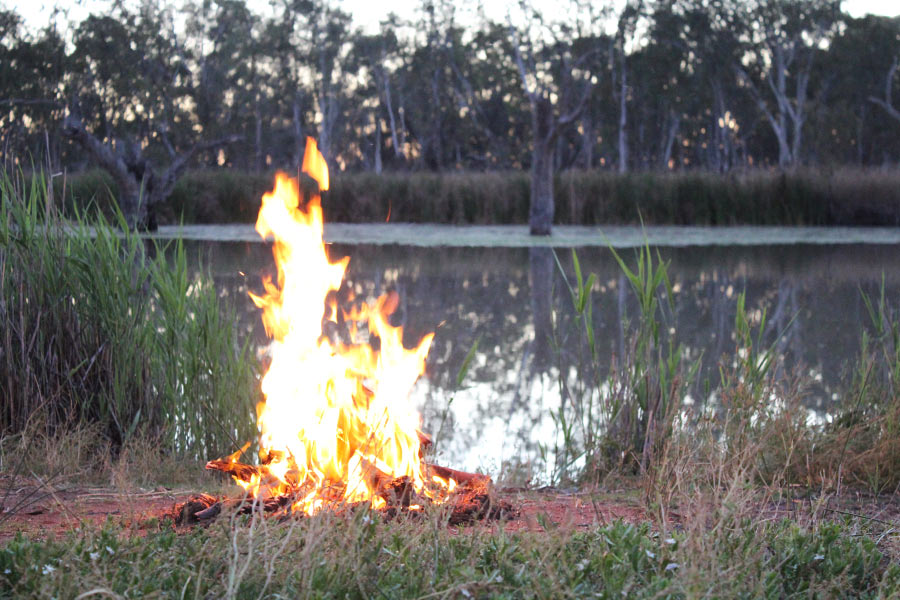 Controlled campfire burning next to a river at dusk