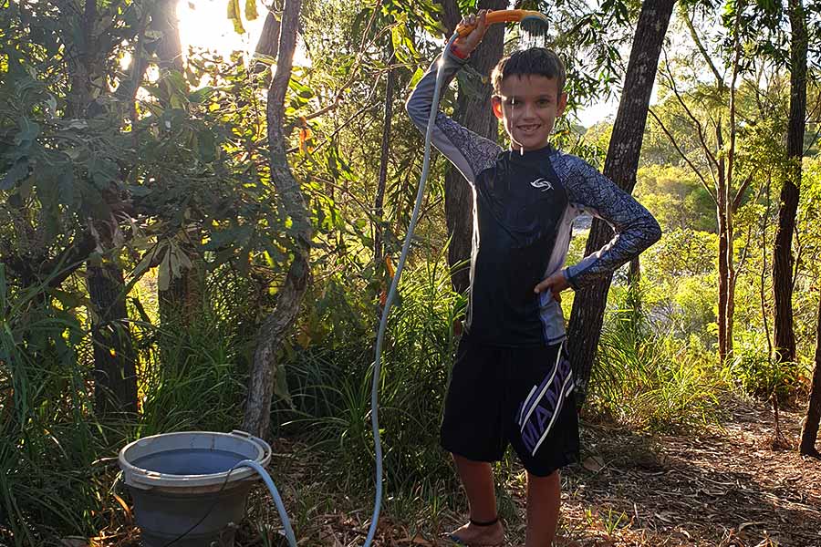 Boy showering outdoors from a hose attached to a hot water unit
