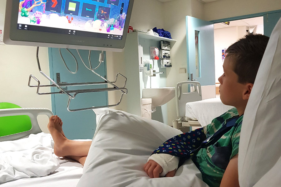 Boy with a broken wrist lying in a hospital bed watching TV