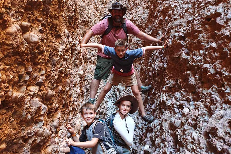 Father and his 3 sons climbing between two tall rocks