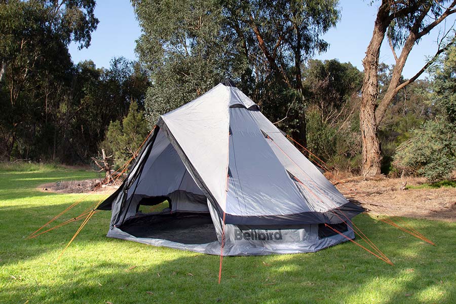 A teepee-style tent set up on grass with trees behind it.