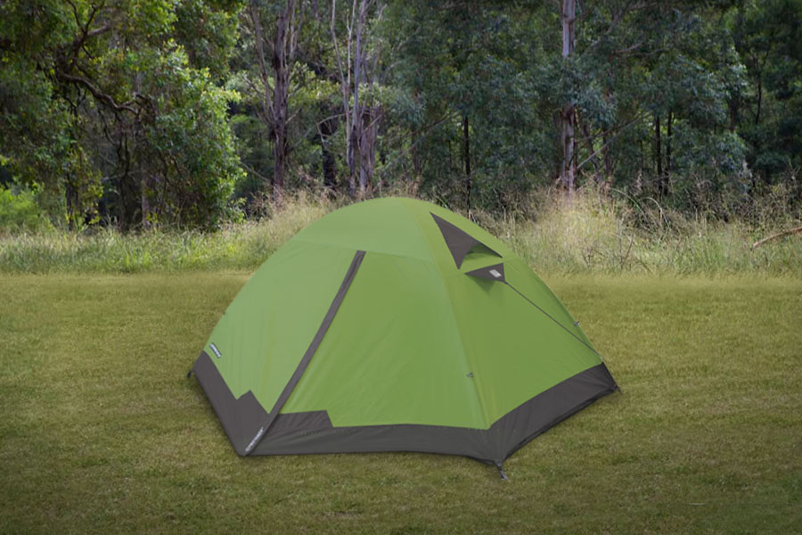 A dome designed hiking tent on green grass with trees in background.