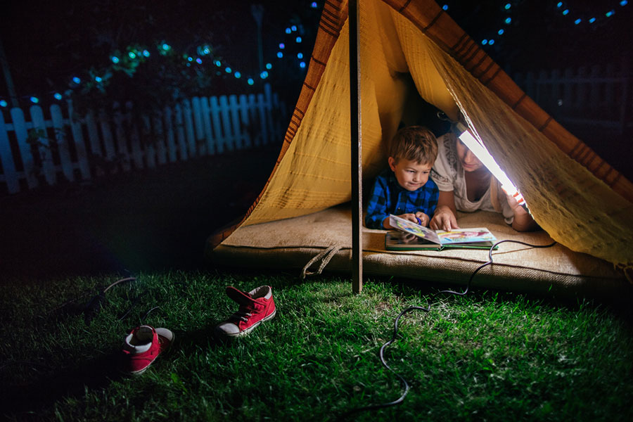 Mother and son reading book inside tent in backyard at night