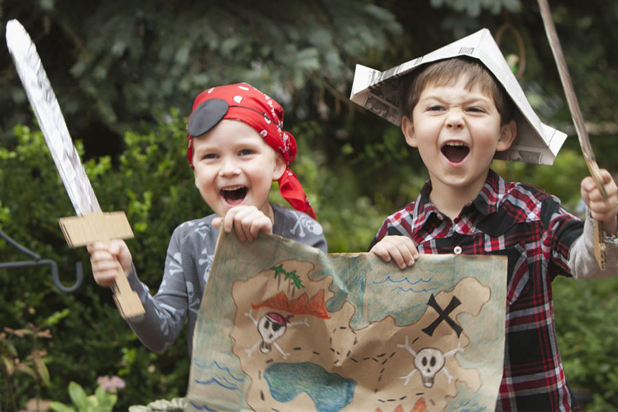 Boys dressed up as pirates holding a treasure map in their backyard
